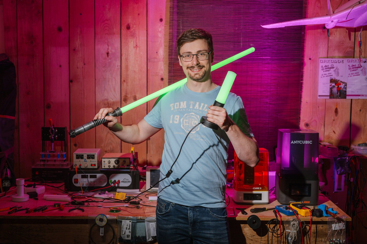 Dr. Frederic Folz holding a green lightsaber and the illuminated FlowGlow Effect Lamp in his workshop.